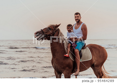 Father and son enjoy riding horses together by the sea. Selective focus Father and son enjoy riding horses together by the sea. Selective focus 95464289