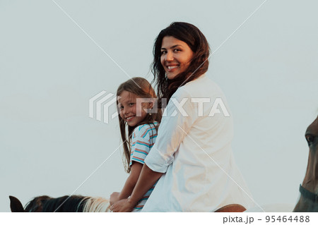 Mother and daughter enjoy riding horses together by the sea. Selective focus  95464488