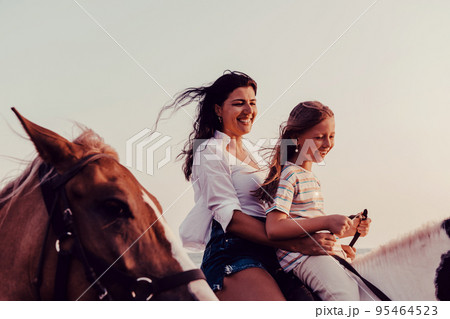 Mother and daughter enjoy riding horses together by the sea. Selective focus  95464523