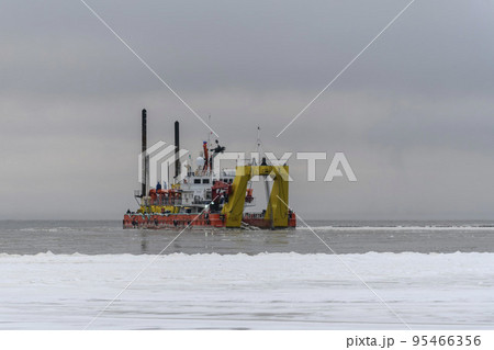 Vessel engaged in dredging at sunset time. Hopper dredger working at sea. Ship excavating material from a water environment. Vessel engaged in dredging at sunset time. Hopper dredger working at sea. Ship excavating material from a water environment. 95466356