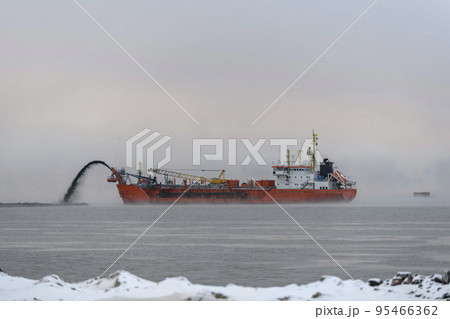 Vessel engaged in dredging at sunset time. Hopper dredger working at sea. Ship excavating material from a water environment. 95466362