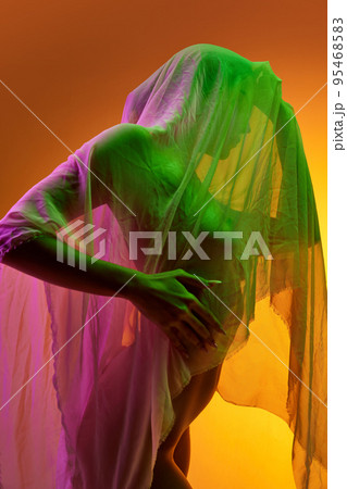 Silhouette of tender woman covered in transparent fabric isolated over orange background in green neon light 95468583