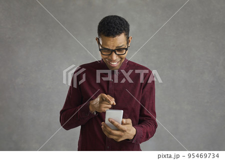 Cheerful afro american guy in stylish wear viewing photos in social networks on mobile 95469734