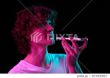 Record voice message. Young handsome boy using smartphone isolated on blackbackground in neon light, filter. Record voice message. Young handsome boy using smartphone isolated on blackbackground in neon light, filter. 95469967