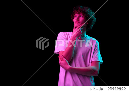 Thinking, dreaming. Half-length portrait of young man with smart facial expression isolated over dark background in purple neon light. Emotions, youth, sales, ad 95469990