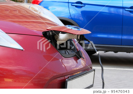 Eco friendly transport concept. Red car is charged on electric charging station in parking lot. Close up. Loading energy. 95470343