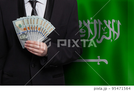 100 US dollar bills money banknotes in hand against flag of Saudi Arabia background 100 US dollar bills money banknotes in hand against flag of Saudi Arabia background 95471564