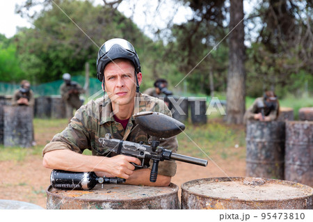 Portrait of man with gun in camouflage on paintball field Portrait of man with gun in camouflage on paintball field 95473810