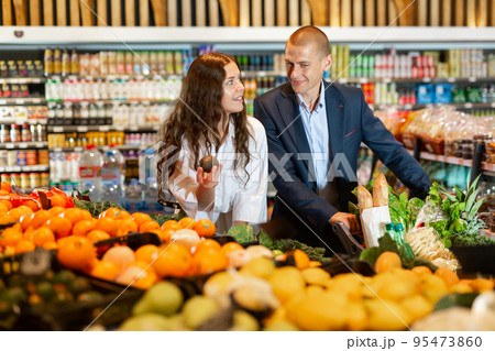 Happy young couple with a grocery cart chooses an avocado in the supermarket 95473860