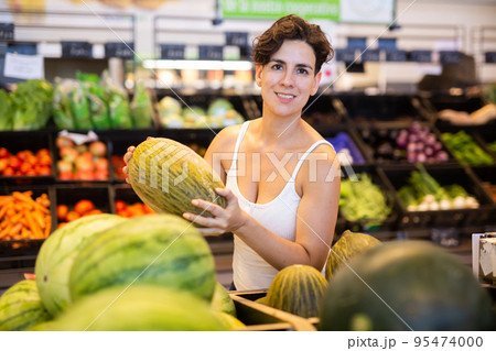 Young Hispanic woman choosing ripe melon in supermarket Young Hispanic woman choosing ripe melon in supermarket 95474000