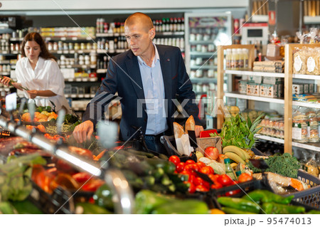 Portrait of a focused young male with a grocery cart in the supermarket Portrait of a focused young male with a grocery cart in the supermarket 95474013