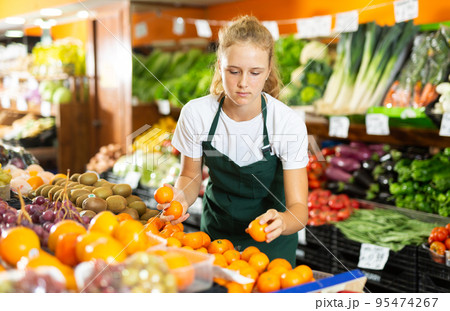 Fifteen-year-old girl who works part-time as a trainee saleswoman puts tangerines Fifteen-year-old girl who works part-time as a trainee saleswoman puts tangerines 95474267