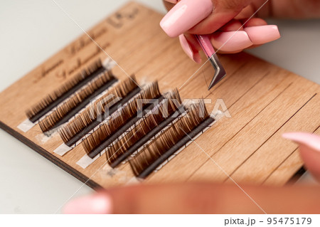 Eyelash extensions, lashmaker tools. Artificial eyelashes on a white tablet and pink silicone brush comb, close up. 95475179