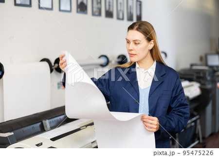 Printing establishment worker examining large piece of paper 95475226