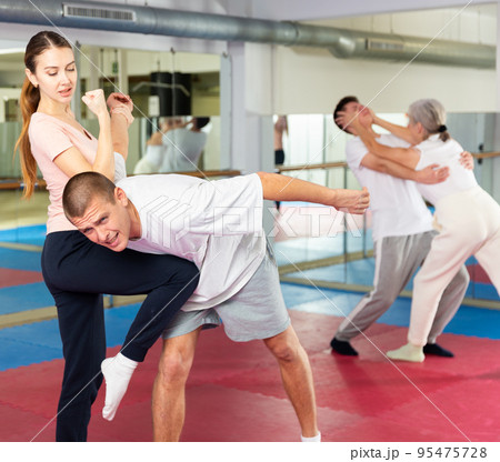 Girl practicing elbow and knee strikes with arm hold to male sparring partner at gym Girl practicing elbow and knee strikes with arm hold to male sparring partner at gym 95475728