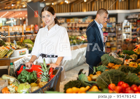 Positive young woman with shopping cart at supermarket 95476142