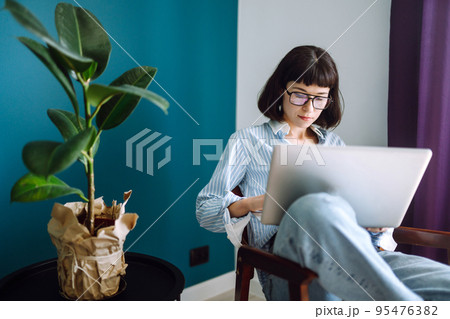Young woman freelancer sit on modern sofa and work on laptop. Education online. Working from home. 95476382