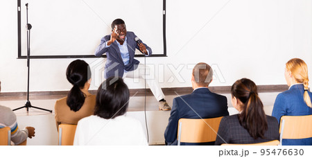 Expressive african american speaker with microphone on conference room stage Expressive african american speaker with microphone on conference room stage 95476630