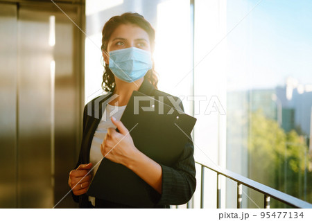 Portrait of businesswoman in protective face mask during virus epidemic while standing near elevator 95477134