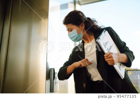 Portrait of businesswoman in protective face mask during virus epidemic while standing near elevator 95477135