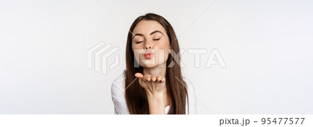 Feminine woman sending air kiss at camera, coquettish flirty pose, kissing, standing over white background 95477577