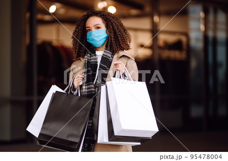 Young woman in protective medical mask with shopping bags 'near mall. Beautiful woman after shopping. Young woman in protective medical mask with shopping bags 'near mall. Beautiful woman after shopping. 95478004