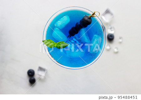 Top view of blue cocktail in martini glass with ice cubes, mint and bluberries Top view of blue cocktail in martini glass with ice cubes, mint and bluberries 95488451