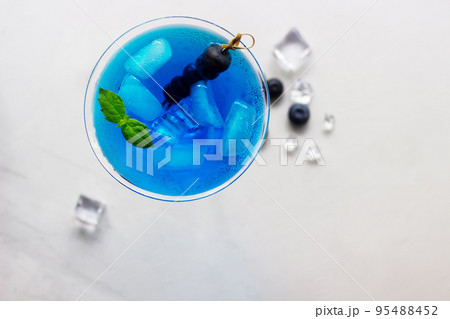 Top view of blue cocktail in martini glass with ice cubes, mint and bluberries Top view of blue cocktail in martini glass with ice cubes, mint and bluberries 95488452