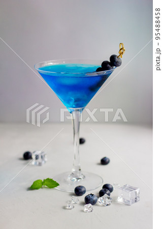 Blue cocktail in martini glass with ice cubes, mint and bluberries 95488458
