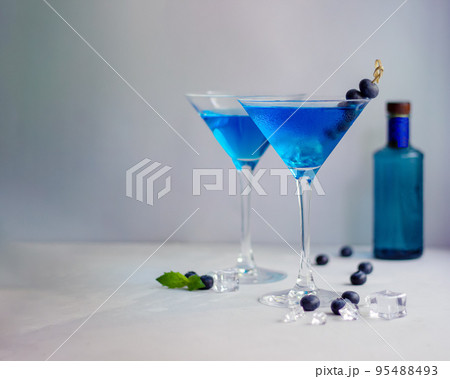 Blue cocktails in martini glass with ice cubes, mint and bluberries and bottle of gin Blue cocktails in martini glass with ice cubes, mint and bluberries and bottle of gin 95488493
