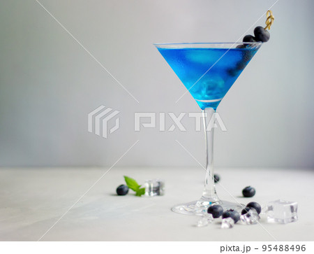 Blue cocktail in martini glass with ice cubes, mint and bluberries 95488496