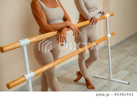 Near the barre, in the choreographic hall, two women in a beige top and leggings are engaged. Near the barre, in the choreographic hall, two women in a beige top and leggings are engaged. 95491442