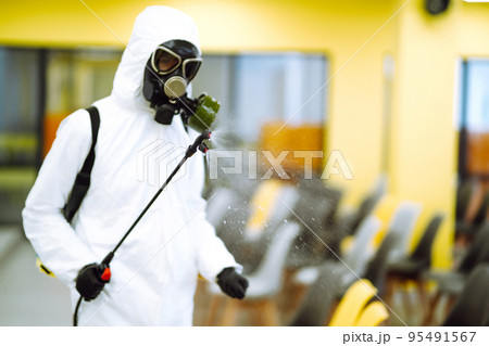 Man wearing protective suit disinfecting assembly hall with spray. Disinfecting of office. COVID-19. Man wearing protective suit disinfecting assembly hall with spray. Disinfecting of office. COVID-19. 95491567