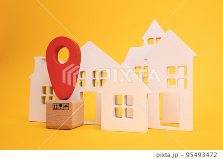 Cardboard boxes and a red position pin in city of white toy house on yellow background. Locating packages and goods. 95493472