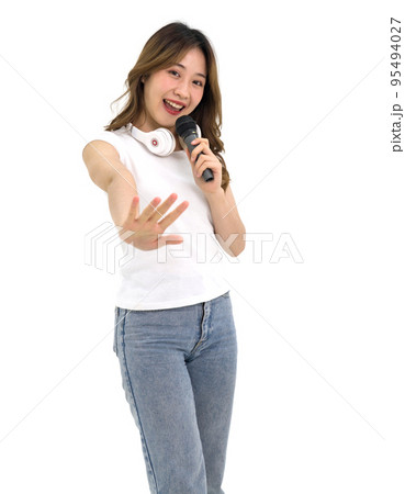 Young asian woman in white t-shirt and jean stand smiling with headphone on her neck, singing with microphone. Portrait on white background with studio light. Isolated Young asian woman in white t-shirt and jean stand smiling with headphone on her neck, singing with microphone. Portrait on white background with studio light. Isolated 95494027