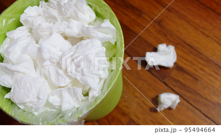 A small garbage bin full with used tissue paper, on a wooden floor. 95494664
