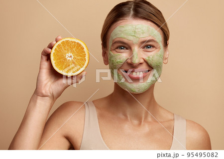 Laughing Face Mask Woman Hold Orange. Positive Woman with Clay Face Mask Laughing Face Mask Woman Hold Orange. Positive Woman with Clay Face Mask 95495082