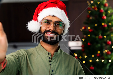 Happy young man wearing santa hat looking at camera celebrating New Year distance online party Happy young man wearing santa hat looking at camera celebrating New Year distance online party 95495218