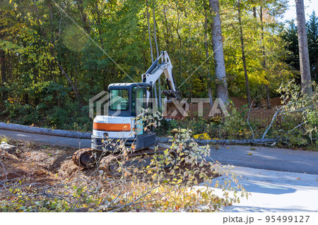 Fallen tree after storm damaged fence after hurricane an uprooted trees fell in street with tractor cleanup raise fallen trees Fallen tree after storm damaged fence after hurricane an uprooted trees fell in street with tractor cleanup raise fallen trees 95499127