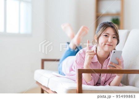 ソファーでスマートフォンを操作する若い女性。 95499863