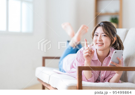 ソファーでスマートフォンを操作する若い女性。 95499864