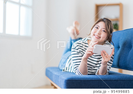ソファーでスマートフォンを操作する若い女性。 95499885