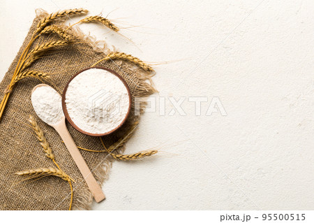 Flat lay of Wheat flour in wooden bowl with wheat spikelets on colored background. world wheat crisis Flat lay of Wheat flour in wooden bowl with wheat spikelets on colored background. world wheat crisis 95500515
