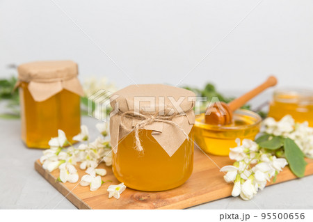 Sweet honey jar surrounded spring acacia blossoms. Honey flows from a spoon in a jar. jars of clear fresh acacia honey on wooden background Sweet honey jar surrounded spring acacia blossoms. Honey flows from a spoon in a jar. jars of clear fresh acacia honey on wooden background 95500656