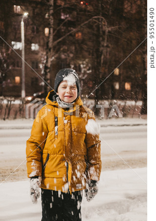 a boy in a yellow jacket plays with snow during a snowfall a boy in a yellow jacket plays with snow during a snowfall 95501490