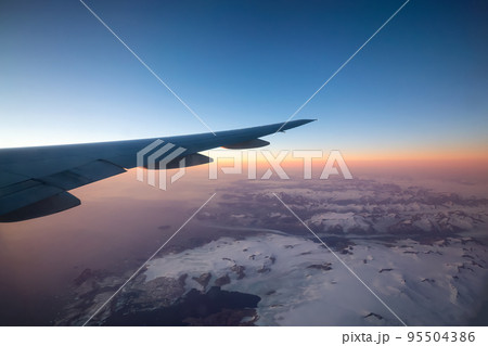 Commercial Aviation Jetplane flying over the ice mountain landscape on the Ocean Coast of Greenland. 95504386