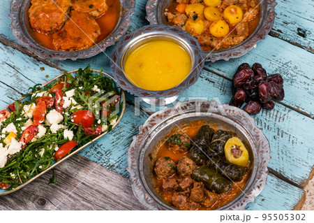 Eid Mubarak Traditional Ramadan Iftar dinner. Assorted tasty food in authentic rustic dishes on wooden blue background. Turkish Bosnian food meat kebab, pita, Sarma, klepe, sogan dolma. Eid Mubarak Traditional Ramadan Iftar dinner. Assorted tasty food in authentic rustic dishes on wooden blue background. Turkish Bosnian food meat kebab, pita, Sarma, klepe, sogan dolma. 95505302