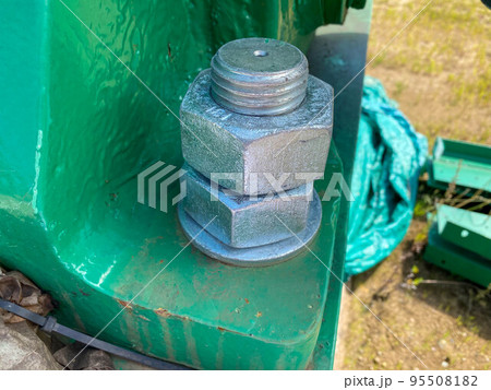 Two nuts are screwed onto a large iron metal stainless mounted threaded bolt. Close view 95508182