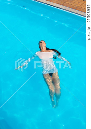 Sensual lady in wet dress standing in pool during summer vacation Sensual lady in wet dress standing in pool during summer vacation 95508956
