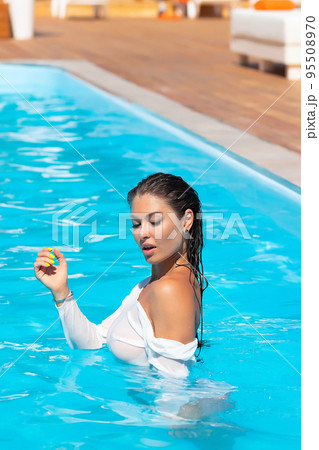 Sensual lady in wet dress standing in pool during summer vacation Sensual lady in wet dress standing in pool during summer vacation 95508970